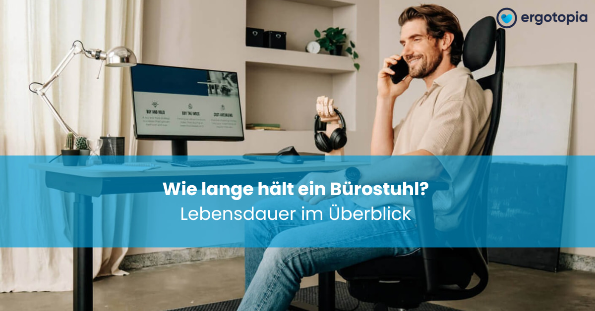 Mann sitzt lächelnd im Bürostuhl und telefoniert am Schreibtisch mit Monitor und Schreibtischlampe
