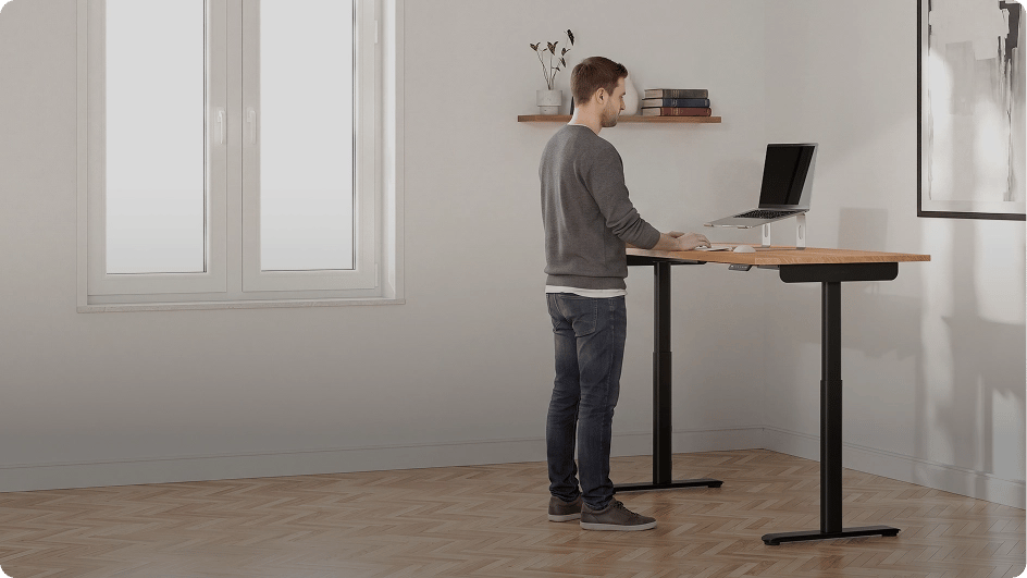 Mann arbeitet ergonomisch im Stehen an dem höhenverstellbaren Schreibtisch Desktopia One im Büro