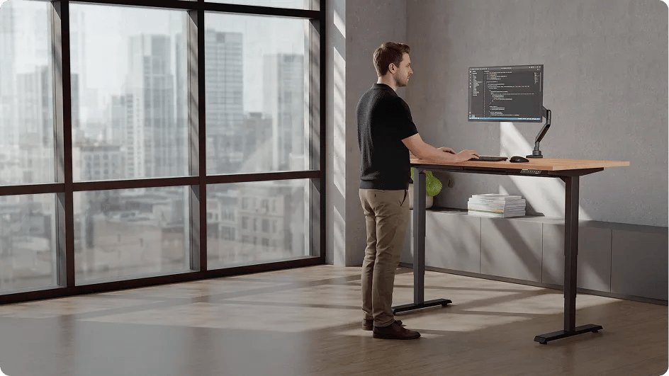 Mann arbeitet konzentriert im Stehen am Premium höhenverstellbaren Schreibtisch Desktopia Pro X vor einem großen Fenster