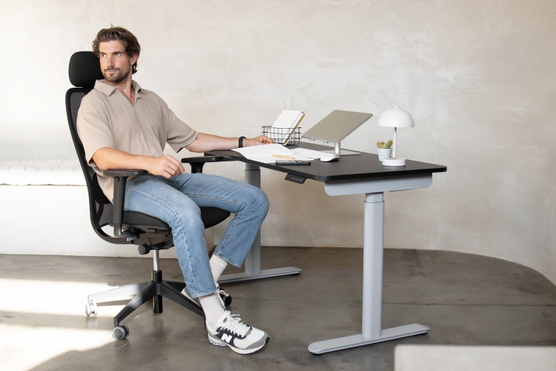 Mann sitzt am ergonomischen Arbeitsplatz mit Laptopständer