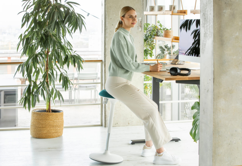 Frau am höhenverstellbaren Schreibtisch auf ergonomischem Stehhocker